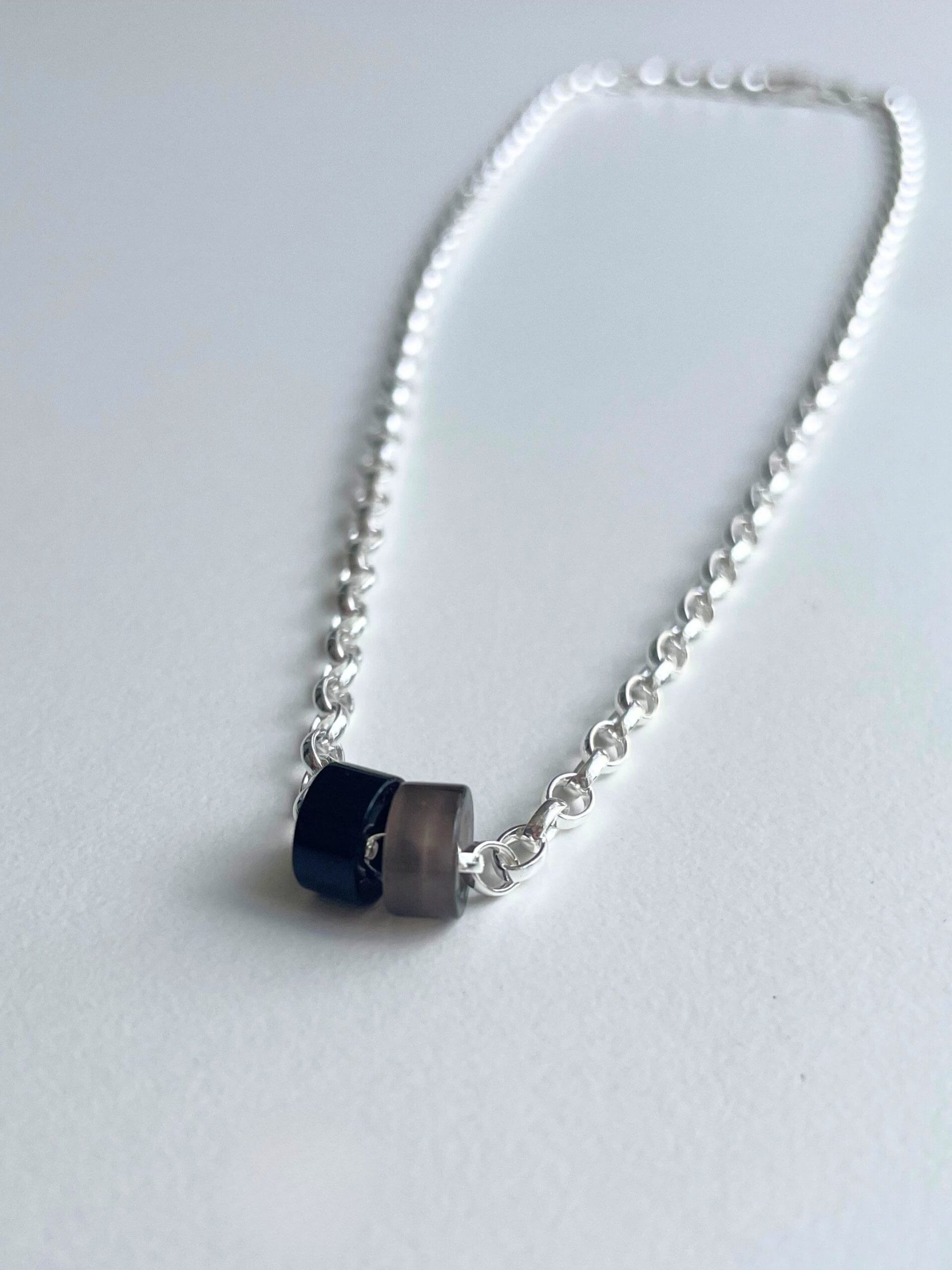 „Timeless sterling silver necklace, 48 cm length, adjustable to 46 cm and 44 cm, with two crystal donut pendants in onyx and smoky quartz; handcrafted from recycled materials, symbolizing grounding, clarity, and transformation.“