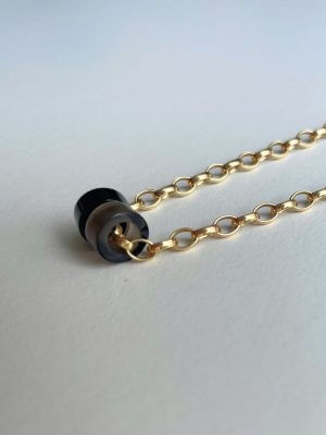 „Timeless 18K gold-plated sterling silver necklace, 48 cm length, adjustable to 46 cm and 44 cm, with two crystal donut pendants in onyx and smoky quartz; handcrafted from recycled materials, symbolizing grounding, clarity, and transformation.“