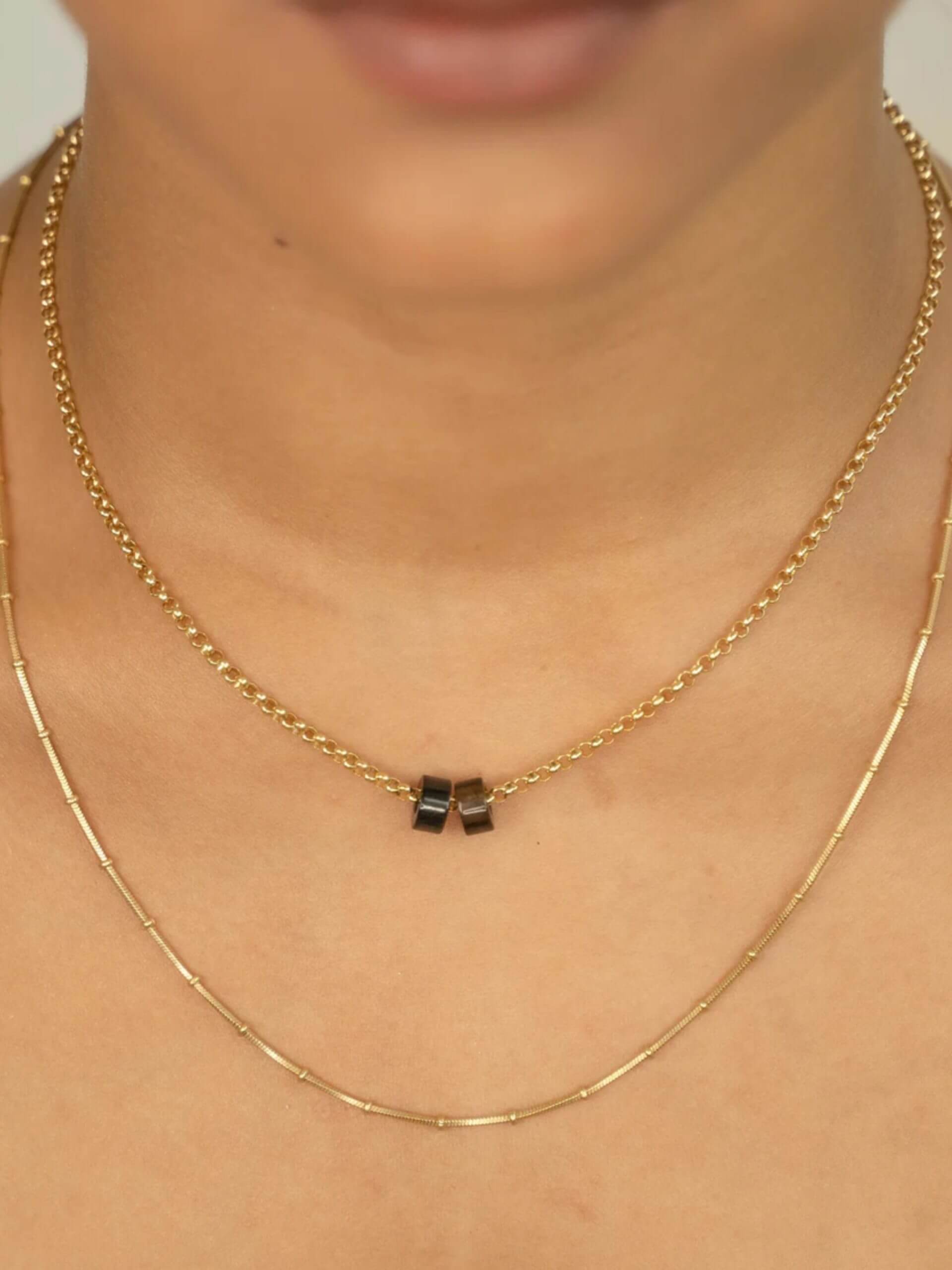 „Timeless 18K gold-plated sterling silver necklace, 48 cm length, adjustable to 46 cm and 44 cm, with two crystal donut pendants in onyx and smoky quartz; handcrafted from recycled materials, symbolizing grounding, clarity, and transformation.“