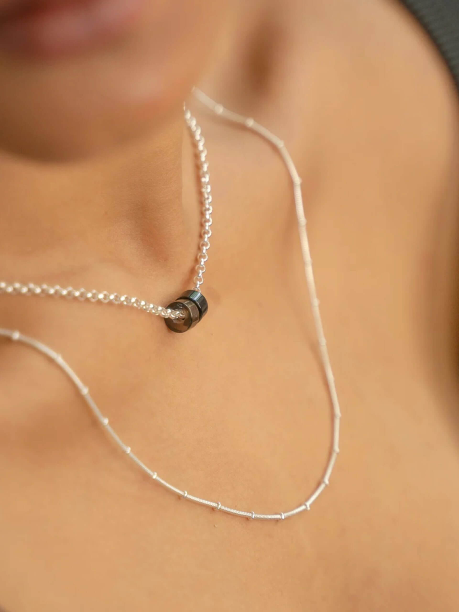 „Timeless sterling silver necklace, 48 cm length, adjustable to 46 cm and 44 cm, with two crystal donut pendants in onyx and smoky quartz; handcrafted from recycled materials, symbolizing grounding, clarity, and transformation.“