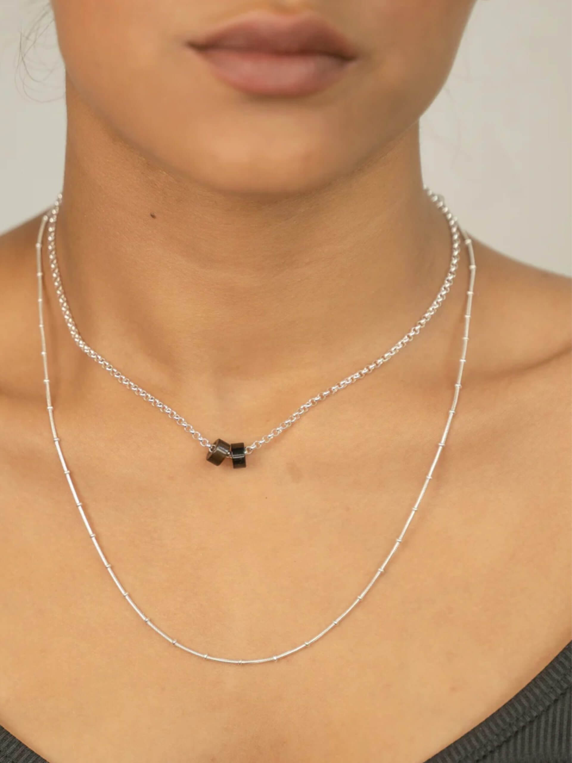 „Timeless sterling silver necklace, 48 cm length, adjustable to 46 cm and 44 cm, with two crystal donut pendants in onyx and smoky quartz; handcrafted from recycled materials, symbolizing grounding, clarity, and transformation.“