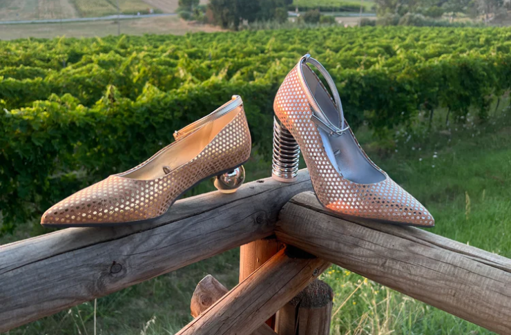 Pink high heels and flat shoes by Fundae with polka dots, displayed on a rustic wooden gate in front of a meadow